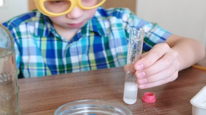Experiments on chemistry at home. Chemical reaction with the release of gas in a test tube in the hands of a surprised boy.