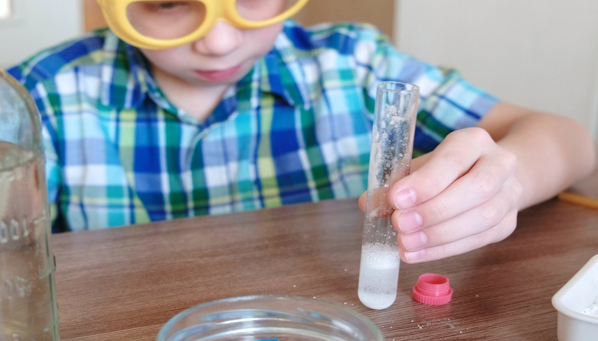 Experiments on chemistry at home. Chemical reaction with the release of gas in a test tube in the hands of a surprised boy.