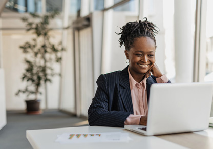 A woman smiles sitting in front of a laptop. 