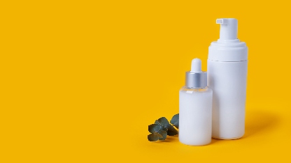 White plastic cosmetics pump and dropper bottles on a yellow background with a tiny branch of eucalyptus 